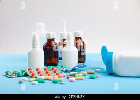 Viele medizinische Medikamente, Thermometer, Spritze, Spray, Flaschen Nase Tropfen, Sirup, verstreut von Pille Flasche bunte Tabletten, Kapseln auf blauem Hintergrund Stockfoto