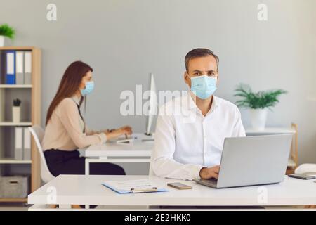 Ernst junger Mann in medizinischen Gesichtsmaske arbeiten in der Firmenbüro mit seinem Kollegen Stockfoto