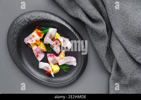 Kalte Vorspeise gesalzener Hering mit gekochten Kartoffeln auf schwarzem Teller auf dunklem Hintergrund, Textilserviette, Nahaufnahme, Draufsicht, flach liegend, Kopierraum, Platz Stockfoto