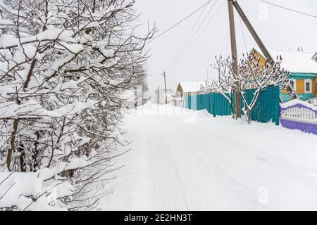 Lange Dorfstraße mit Schnee bedeckt, Schnee auf Bäumen, Häuser im Dorf, Strommast im Winter Stockfoto