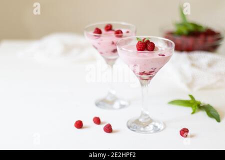 Köstliches Dessert, Käsekuchen mit frischen Himbeeren und Buttercreme-Mousse im Glas auf einem weißen Tisch. Speicherplatz kopieren Stockfoto