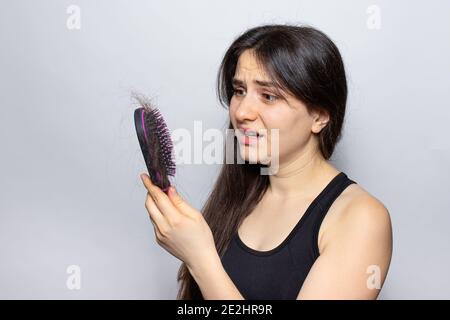 Das Mädchen hält einen Kamm für Haare mit gefallenen Haaren. Haarausfall, Haarpflege Stockfoto