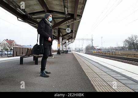 MOTALA, SCHWEDEN- 13. DEZEMBER 2020: Eine Person mit Gesichtsmaske wartet auf dem Bahnsteig in Östgötatrafiken Pendlerzug während dieser Corona-Zeiten. Stockfoto