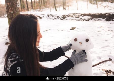 Junges Mädchen, das einen Schneemann auf einem verschneiten Wald baut. Stockfoto