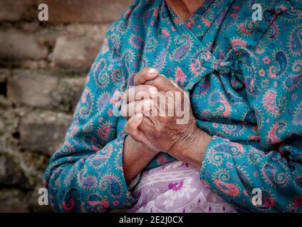 Unbekannte ältere Frau mit blauen Tüchern, die ihre zerknitterten Hände kreuzten. Alterungsprozess Stockfoto