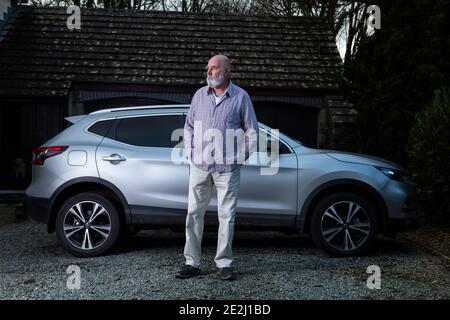 Lässig gekleideter älterer Mann mit seinem silbernen Auto. Stockfoto