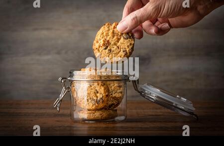 Hand greift nach einem Keks in einem Glas. Hafer und Rosinen hausgemachte Kekse Stockfoto