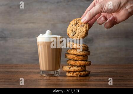 Coffee Latte in einem Glas mit einer Hand nach Ein Cookie auf einem Holztisch Stockfoto