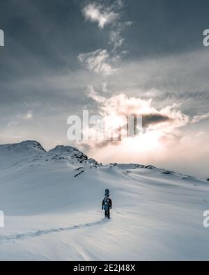 Vertikale Aufnahme einer Person, die in einer bergigen Gegend wandert Bedeckt von Schnee unter dem düsteren Himmel Stockfoto