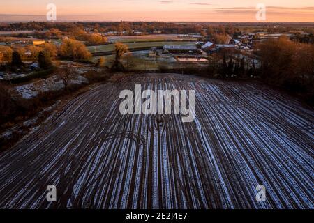 Luftaufnahme von gefrorenen gepflügten Feld mit schönen orange Himmel im Hintergrund, späten Sonnenuntergang im Winter Stockfoto