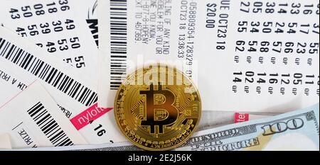Eine Bitcoin Goldmünze auf Lotterielose und Geldscheine platziert. Stockfoto
