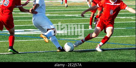 Zwei männliche High School-Fußballspieler kämpfen sich während eines Spiels auf einem grünen Rasenplatz um den Ball.