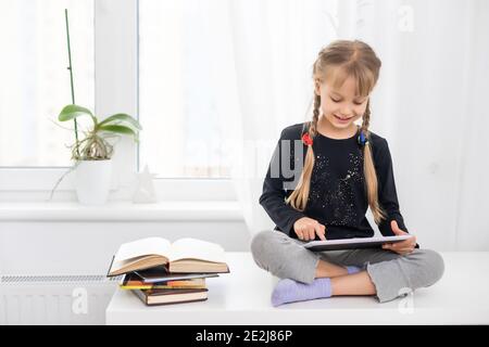 Lächelnde junge weibliche Kinder mit digitalen Tablet-Pad beobachten Online-E-Learning-Video zum Englischlernen zu Hause Stockfoto