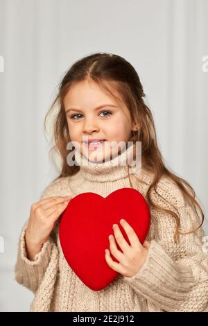 valentinstag. Niedliche kleine Mädchen hält rotes Herz gegen weiße Wand. Stockfoto