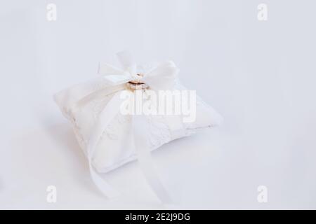 Zwei goldene Verlobungsringe an einem weißen kleinen Dekor-Kissen Kissen mit Band Stockfoto