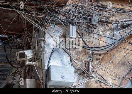 Eine Überwachungskamera schützt ein Grundstück inmitten eines wirren Durcheinander von elektrischen Kabeln, die es einem Brandrisiko aussetzt. Stockfoto