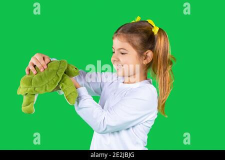 Vorschulmädchen niedlich lächelnd und hält eine weiche grüne Schildkröte auf einem grünen Hintergrund. Stockfoto