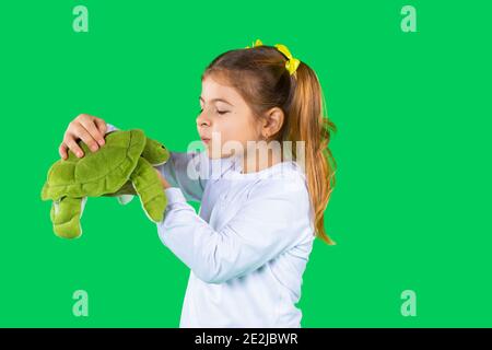 Ein Mädchen mit Zöpfen hält eine weiche Schildkröte in den Händen und will sie küssen. Grüner Hintergrund. Seitenraum. Stockfoto