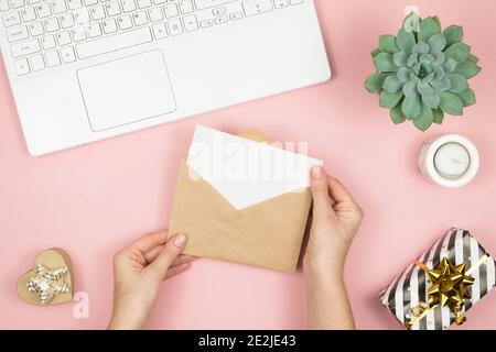 Womans Hände halten Handwerk Umschlag mit Copyspace auf rosa pastellfarbenen Tisch Draufsicht. Flat Lay Zusammensetzung für Valentinstag. Alles gute für den Tag der Frau Stockfoto