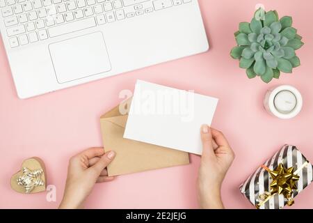Womans Hände halten Handwerk Umschlag mit Copyspace auf rosa pastellfarbenen Tisch Draufsicht. Flat Lay Zusammensetzung für Valentinstag. Alles gute für den Tag der Frau Stockfoto