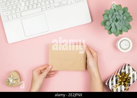 Womans Hände halten Handwerk Umschlag mit Copyspace auf rosa pastellfarbenen Tisch Draufsicht. Flat Lay Zusammensetzung für Valentinstag. Alles gute für den Tag der Frau Stockfoto