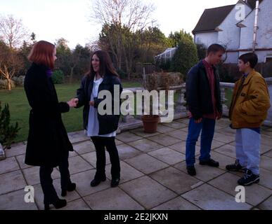 Teenage Mädchen schütteln Hände greetiing einander mit zwei Jungen Chatten hinter im Garten Surrey England Stockfoto