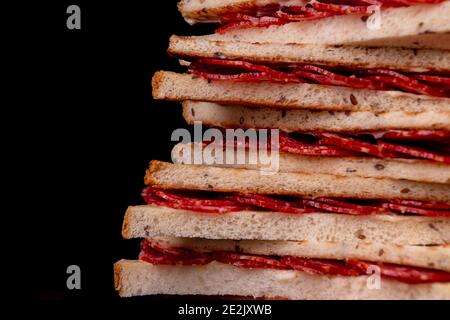 Heep von Sandwiches getoastetes Brot und Salami auf schwarz. Fastfood ungesunde Konzept. Copy space Stockfoto