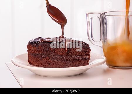 Stück sachertorte sachertorte kuchen auf weißem Teller. Gießen Schokolade aus Löffel, cuo von Kaffee mit Milch Stockfoto