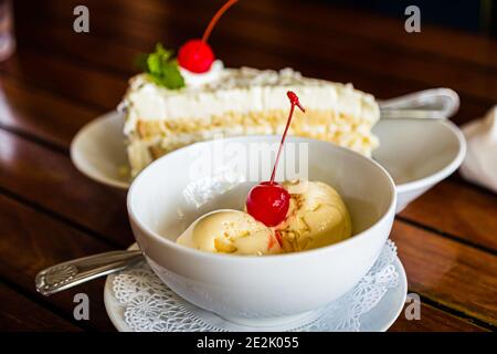Das Aquarium-Restaurant am Magazine Beach in Calliste, Grenada, serviert eine Scheibe Sahnetorte und zwei Kugeln Eis zusammen auf dem Tisch, beide mit einer Maraschino-Kirsche garniert. Stockfoto