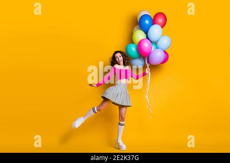 In voller Länge Körpergröße Foto von lustigen hübschen jungen Mädchen Hochspringen hoch halten Luftballons lächelnd lachen isoliert auf Leuchtend gelbe Farbe Stockfoto