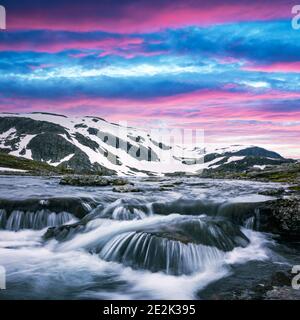 Farbenfroher Sonnenaufgang auf schneebedeckten norwegischen Bergen und klarem Fluss in der Nähe des berühmten Aurlandsvegen (Bjorgavegen), Bergstraße, Aurland, Norwegen. Stockfoto