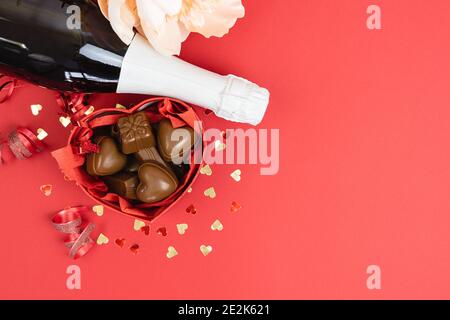Champagner-Flasche mit Schachtel Pralinen auf rotem Hintergrund Copy Space, Valentinstag, Muttertag, Jubiläum, Geburtstag. Stockfoto
