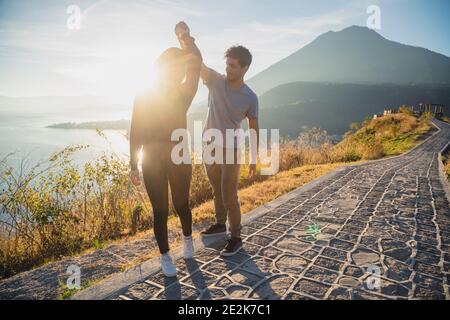 Junges Paar tanzt mit Blick auf den Atitlan See bei Sonnenaufgang - Reisen Verliebtes Paar am Aussichtspunkt am See in Guatemala - sonnenaufgang Seenlandschaft Stockfoto