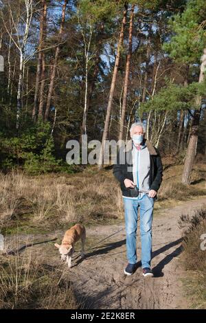 Älterer Mann mit Gesichtsmast beim Wandern mit dem Hund im Naturwald Stockfoto