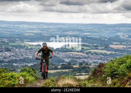 Eine Frau fährt mit dem Mountainbike bergauf auf auf einem Trail in den Hügeln über pontypool und Cwmbran in Torfaen, Wales. Stockfoto