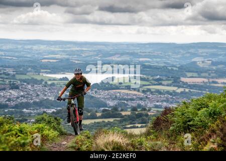 Eine Frau fährt mit dem Mountainbike bergauf auf auf einem Trail in den Hügeln über pontypool und Cwmbran in Torfaen, Wales. Stockfoto