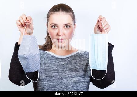 Junge Frau hält zwei Masken Einweg und wiederverwendbar auf weißem Hintergrund. Stockfoto