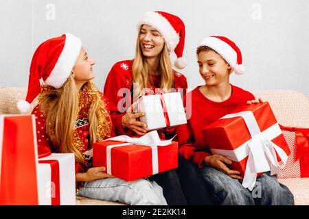 Frohes neues Jahr und frohe Weihnachten! Glückliche Familie, eine junge Mutter mit Kindern, trägt weihnachtsmann Hüte, grüßt das neue Jahr und gibt einander Chr. Stockfoto