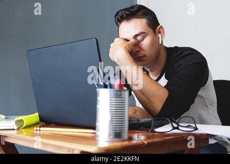 Gestresster und müder kaukasischer junger Mann, der von zu Hause aus sitzt Auf einem Schreibtisch mit der Hand im Gesicht Stockfoto
