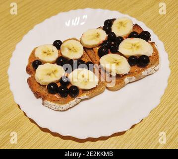 Ein gesundes Dessert zum Frühstück, Mittag- oder Abendessen dunkles Brot mit Erdnussbutter, schwarzer Johannisbeere und Bananenscheiben Stockfoto