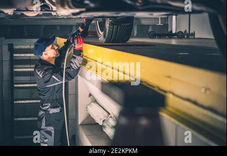 Caucasian Professional Car Mechanic mit Taschenlampe Performing Vehicle Undercarriage Überprüfen Sie auf der Suche nach potenziellen Problemen mit der Federung. Kfz-Pr Stockfoto