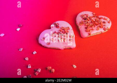 Zwei Paar Kekse Rotes Herz geformt für valentinstag, getönt in trendigen Neon-Hintergrund. Draufsicht. Leerzeichen für Text. Leckerbissen Stockfoto