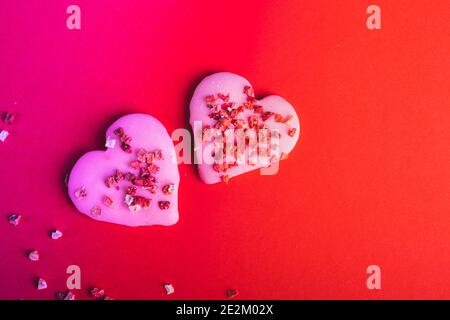 Zwei Paar Kekse Rotes Herz geformt für valentinstag, getönt in trendigen Neon-Hintergrund. Draufsicht. Leerzeichen für Text. Leckerbissen Stockfoto