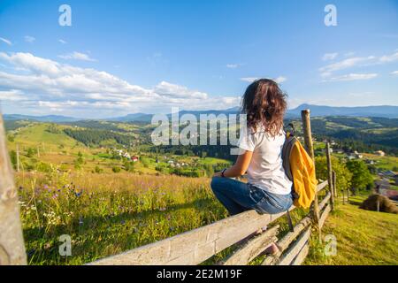 Happy Gorgeous Mädchen genießen Hügel Blick sitzt in Blumenfeld auf dem Hügel mit atemberaubender Naturlandschaft. Stockfoto