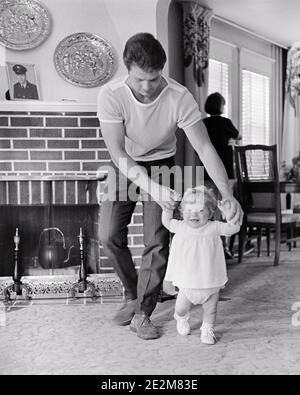 60ER JAHRE MANN VATER HILFT HALTEN UNTERSTÜTZUNG BABY MÄDCHEN TOCHTER KLEINKIND MACHEN SIE DIE ERSTEN SCHRITTE ZU FUSS IM WOHNZIMMER - B23320 HAR001 HARS URBAN SCHRITTE LERNEN ALTE ZEIT NOSTALGIE ALTE MODE 1 JUVENILE STIL LACHEN TAKE BALANCE TEAMWORK KLEINKIND FREUDE LEBENSGEFÜHL ELTERNSCHAFT FRAUEN GESUNDHEIT HEIM LEBEN KOPIEREN RAUM IN VOLLER LÄNGE TÖCHTER PERSONEN CARING MÄNNER VÄTER B & W ZIELE GLÜCK FRÖHLICH VÄTER AUFREGUNG FÜHRUNG IN UP LÄCHELT KONZEPTUELLE FREUDIGE UNTERSTÜTZUNG FÜR WACHSTUM JUGENDLICHE MITTLEREN ERWACHSENEN MID-ADULT MANN ZWEISAMKEIT BABY MÄDCHEN SCHWARZ UND WEISS KAUKASISCHEN ETHNIE HAR001 ALTMODISCH Stockfoto