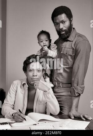 70ER JAHRE PORTRÄT AFROAMERIKANISCHEN FAMILIE VATER STEHEND HÄLT BABY MUTTER SITZENDE ÜBERPRÜFUNG BUDGET ALLE BLICK AUF KAMERA - B26006 HAR001 HARS MÜTTER ALTE ZEIT NOSTALGIE ALTE MODE BART 1 JUGENDLICH KOMMUNIKATION JUNGE ERWACHSENE TEAMARBEIT KLEINKIND SÖHNE FAMILIEN LIFESTYLE FRAUEN VERHEIRATET STUDIO ERSCHOSSEN EHEGATTEN EHEMÄNNER ZU HAUSE LEBEN SITZEND KOPIE RAUM FREUNDSCHAFT HALF-LENGTH DAMEN PERSONEN PFLEGE MÄNNER VÄTER B&W PARTNER AUGENKONTAKT DOKUMENTE AFROAMERIKANER AFROAMERIKANER VÄTER SCHWARZE ETHNIE GESICHTSHAAR AN DER KAMERA ÜBERPRÜFUNG BABY JUNGE BÄRTE ZUSAMMENARBEIT JUVENILES MÜTTER ZWEISAMKEIT FRAUEN JUNG ERWACHSENER MANN Stockfoto