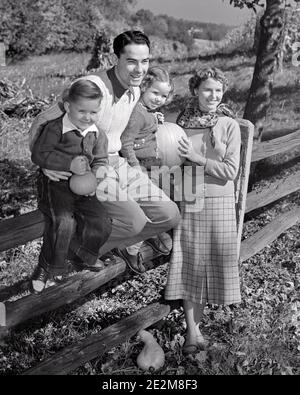 50S LÄCHELNDE FAMILIE IM HERBST HÄLT KÜRBISSE VATER TOCHTER UND SOHN SITZT AUF HÖLZERNEN GESPALTENEN SCHIENE ZAUN MUTTER STEHEND - C4912 HAR001 HARS ZAUN VIER HERBST MAMA HOLZBEKLEIDUNG NOSTALGISCH HERBST PAAR 4 BLÄTTER MÜTTER ALTE ZEIT NOSTALGIE BRUDER ALT MODE SCHWESTER 1 JUGENDLICH STIL SÖHNE ERFREUT FAMILIEN FREUDE LIFESTYLE ZUFRIEDENHEIT FRAUEN VERHEIRATET BRÜDER LÄNDLICHEN EHEGATTEN EHEMÄNNER ZU HAUSE LEBEN NATUR COPY SPACE FREUNDSCHAFT IN VOLLER LÄNGE HALBLANG DAMEN TÖCHTER PERSONEN MÄNNER GESCHWISTER SCHWESTERN VÄTER LANDWIRTSCHAFT B&W PARTNER GLÜCK FRÖHLICH KÜRBISSE STILE UND VÄTER AUSSEN HERBST SAISON STOLZ GESCHWISTER Stockfoto