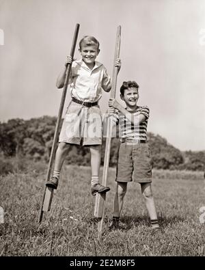 1930ER JAHRE 1940ER JAHRE ZWEI JUNGEN IN SHORTS SPIELEN ZUSAMMEN IM FREIEN EIN GEHEN AUF STELZEN BLICK AUF DIE KAMERA DER ANDERE HILFT GLEICHGEWICHT - B5584 HAR001 HARS FREUDE ZUFRIEDENHEIT BRÜDER LÄNDLICHE GESUNDHEIT HOME LEBEN KOPIEREN RAUM FREUNDSCHAFT VOLLE LÄNGE KÖRPERLICHE FITNESS MÄNNER RISIKO GESCHWISTER B&W SOMMERZEIT BLICKKONTAKT AKTIVITÄT STELZEN GLÜCK KÖRPERLICH FRÖHLICH ABENTEUER ENTDECKUNG STÄRKE AUFREGUNG ERHOLUNG STOLZ GESCHWISTER LÄCHELT FLEXIBILITÄT FREUNDLICH FREUDIGE MUSKELN ZUSAMMENARBEIT WACHSTUM JUVENILES PRE-TEEN PRE-TEEN JUNGE SAISON STELZEN ZWEISAMKEIT SCHWARZ-WEISSE KUMPELS KAUKASISCHE ETHNIE HAR001 Stockfoto