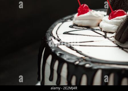 Weißer Kuchen mit dunkler Schokolade und einigen süßen Kirschen mit Schwarzer Hintergrund Stockfoto