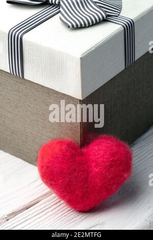 Rote Wolle handgemachte Herz steht neben Geschenkbox auf der Weiße Holzbretter Stockfoto